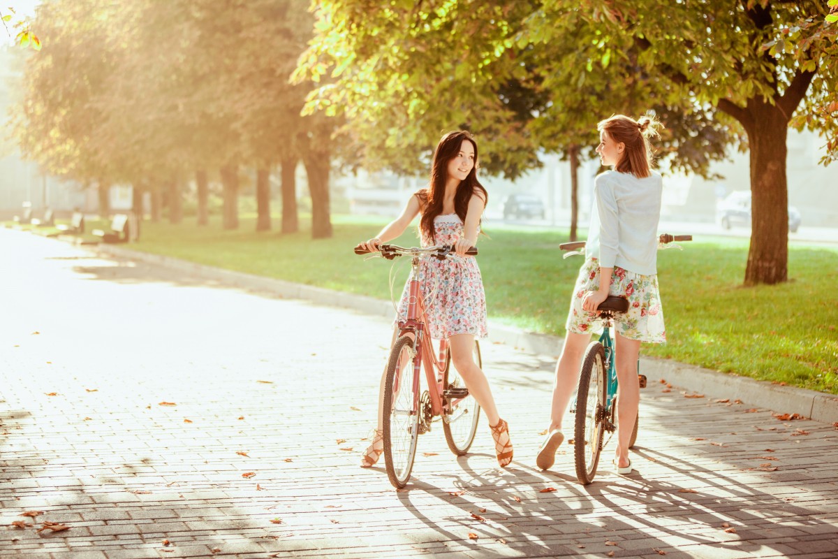 C'est l'été, deux jeunes filles à bicyclette se regardent et se parlent dans un parc.
