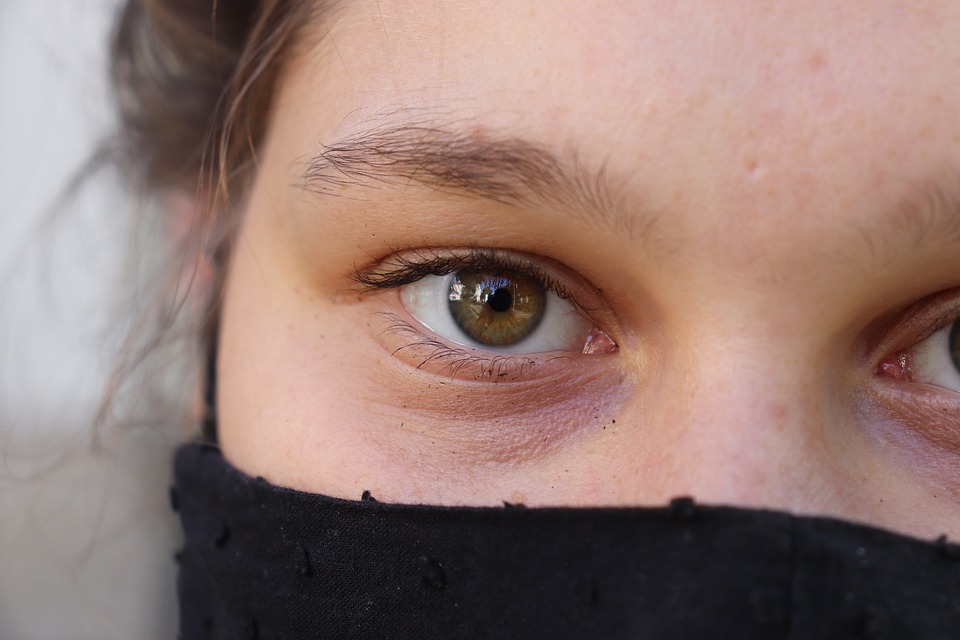 Une jeune fille de face, le moitié de son visage est caché d'une écharpe noire. Elle a les yeux verts et le regard determiné. 